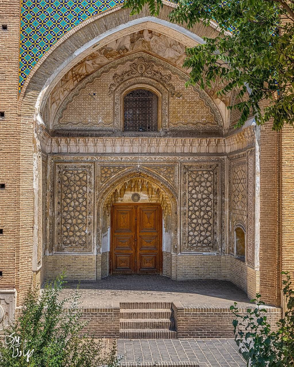 سردر آجری ورودی بنا با تزئینات کاشی‌کاری و درِ چوبی سنتی